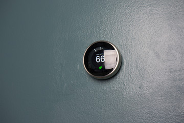 Smart thermostat in home displaying 66 degrees. Temperature adjustment of thermostat on blue wall...