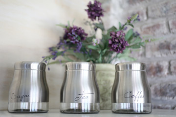 Interior decoration.  Tea, coffee and sugar jars, purple flowers on a shelf.