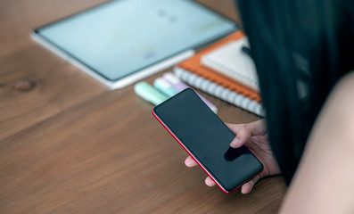 Cropped shot of woman using smartphone while sitting at office desk.