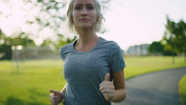 Pretty blonde woman runs on park path, revealing sun flares behind slow motion