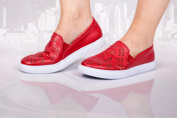 Lady wearing red shoes reflecting in a puddle of water with a cityscape in the background.