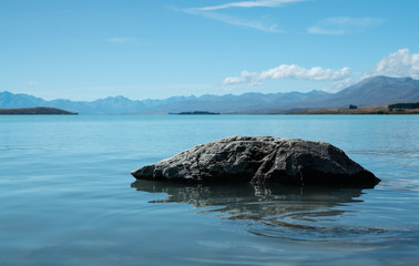Rock in lake with mountains and clouds at Lake Tekapo New Zealand