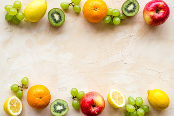 Fresh fruits background with citruses, apple, kiwi and grape on beige table top-down frame copy space