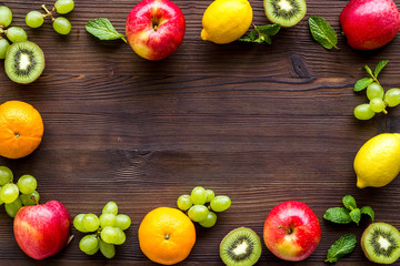 Fresh fruits background with citruses, apple, kiwi and grape on wooden table top-down frame copy space