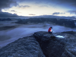 Hiker girl sit in dark night above clouds and wait for sunrise