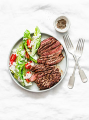 Beef steak and romaine cherry tomatoes yogurt dressing salad on a light background, top view