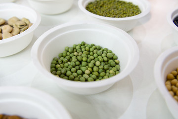 Green peas in a white plastic plate. Around in the same plates are various seeds, nuts and beans.