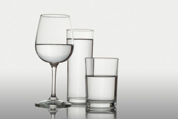 Vasos de cristal y copa con agua sobre una superficie y fondo blanco