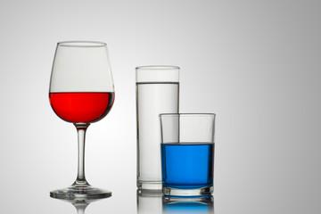 Copa y vasos de cristal con un fondo blanco y bebidas de diferentes tipos y colores, con composiciones atractivas