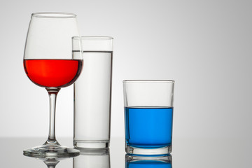 Copa y vasos de cristal con un fondo blanco y bebidas de diferentes tipos y colores, con composiciones atractivas