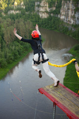 Girl, tied on a safety rope, jumps from a great height against the background of a river....