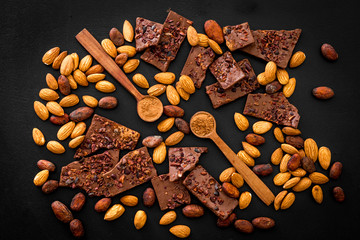 Sweets background with chocolate pieces and nuts on black table top-down