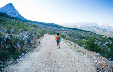 Fototapeta premium A woman with a backpack is walking along a mountain road.