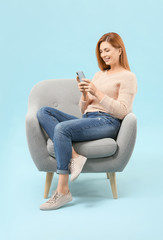 Fototapeta na wymiar Beautiful woman with mobile phone sitting in armchair against color background