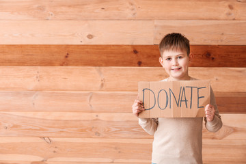 Little boy holding cardboard with text DONATE on wooden background