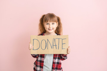 Little girl holding cardboard with text DONATE on color background