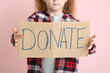 Little girl holding cardboard with text DONATE on color background