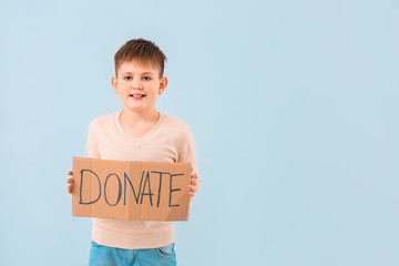Little boy holding cardboard with text DONATE on color background