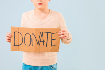 Little boy holding cardboard with text DONATE on color background