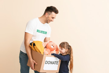 Volunteer with donations for orphans and little child on color background