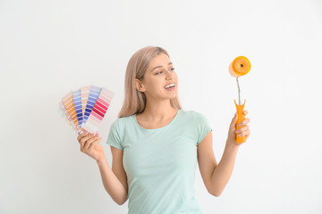 Young woman with color swatches and paint roller on white background