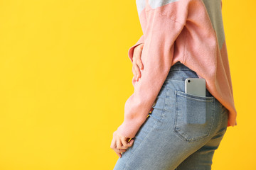 Beautiful young woman with mobile phone in pocket on color background, closeup