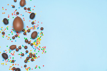 Chocolate eggs and candies on color background