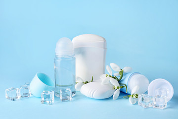 Different deodorants and flowers on color background
