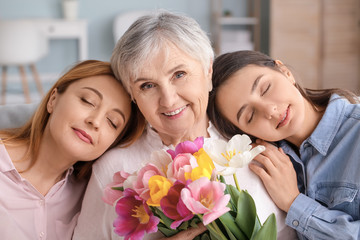 Mature woman with her adult daughter, mother and beautiful flowers at home