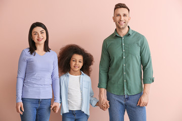 Happy couple with little adopted girl on color background