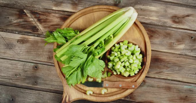 A bunch and pieces of fresh celery on a wooden cutting Board slowly rotate.