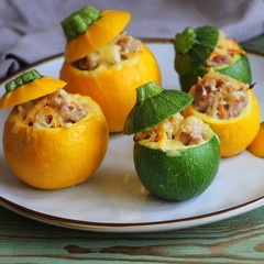 Yellow and green zucchini baked with a filling close-up on a plate. Roasted round zucchini stuffed with minced meat, vegetables, and cheese