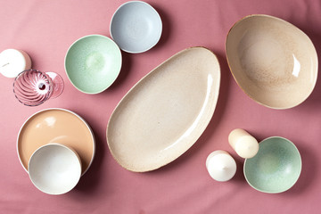 Light pastel colored tableware set: empty serving plates, bowls, candles on pink shabby background. Copy space. Top view. Family dinner concept
