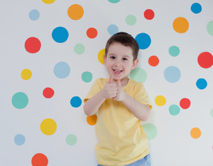 Fototapeta na wymiar Toddler boy on a background of wall with colorful circles. Boy giving thumbs up