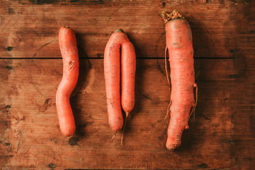 Ugly misshapen carrots on wooden background. Concept of zero waste production. Top view. Copy...