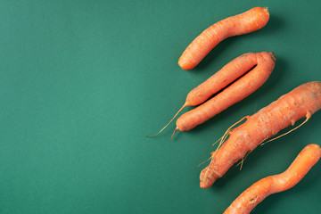 Ugly misshapen carrots on green background. Concept of zero waste production. Top view. Copy space....