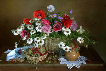 A bouquet of daisies, poppies in a basket and berries on the table.