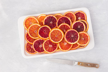 Sliced blood oranges circles on white plate on light background, top view, horizontal