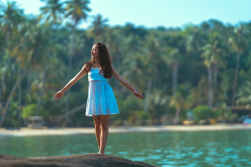 asian girl in white dress a holiday relax time in white dress by standing on stone in the sea with sunday light and blue sky in relaxing and freedom concept with blur coconut background