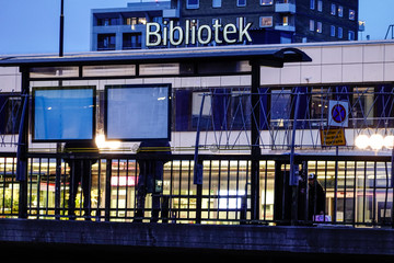 Stockholm, Sweden People wait at a bus stop in Hogdalen and a sign for the public library.
