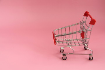 Small trolley with a shopping basket for buy in store on a pink background.