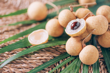 Longan fruits over palm leaves on rattan background. Copy space. Dimocarpus longan. Bunch of exotic longans. Tropical food concept.
