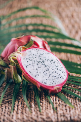 White pitahaya or dragon fruit with palm leaves on rattan background. Copy space. Creative design...