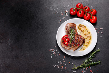 Fototapeta na wymiar Fresh delicious juicy steak on the bones with vegetables and spices against a dark background