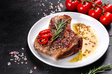 Fresh delicious juicy steak on the bones with vegetables and spices against a dark background
