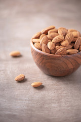 Almond nuts in wooden bowl on wood textured background. Copy space. Superfood, vegan, vegetarian food concept. Macro of almond nut texture, selective focus. Healthy snack