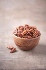 Pecan nuts in wooden bowl on wood textured background. Copy space. Superfood, vegan, vegetarian food concept. Macro of pecan nut, selective focus. Healthy snack