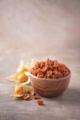 Dried physalis in wooden bowl and fresh berries on wood textured background. Copy space. Superfood, vegan, vegetarian food concept. Macro of inca berries, selective focus. Healthy snack.