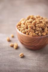 White dried mulberry in wooden bowl on wood textured background. Copy space. Superfood, vegan, vegetarian food concept. Macro of mulberry berries, selective focus. Healthy snack.