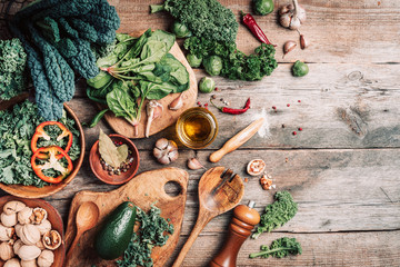 Orgnic healthy vegan food cooking ingredients. Top view. Copy space. Green vegetables, seeds, avocado, nuts, kale, spices, salt, wooden utensils on wood background. Clean eating food, zero waste